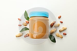 Jar with peanut butter, peanuts and leaves on white background