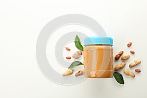 Jar with peanut butter, peanuts and leaves on white background