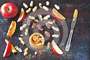 Jar of peanut butter, peanuts in a peel, apple slices and a knife.