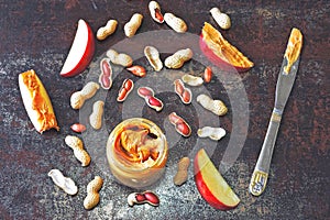 Jar of peanut butter, peanuts in a peel, apple slices and a knife.