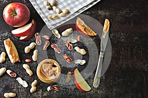 Jar of peanut butter, peanuts in a peel, apple slices and a knife.