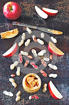 Jar of peanut butter, peanuts in a peel, apple slices and a knife.