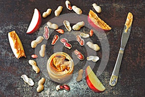 Jar of peanut butter, peanuts in a peel, apple slices and a knife.