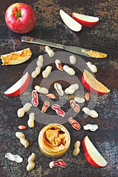 Jar of peanut butter, peanuts in a peel, apple slices and a knife.