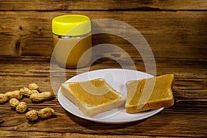Jar of peanut butter and plate with two sandwiches with peanut butter on wooden table
