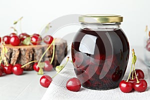 Jar of pickled cherries and fresh fruits on light table, closeup