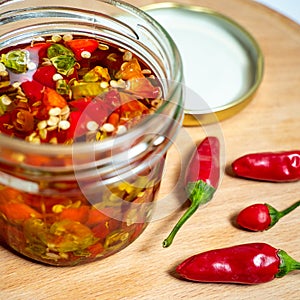 Jar with preserved red hot chilly peppers and peppers near