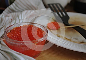 a jar of red caviar close-up and thin pancakes, a golden spoon with caviar and a kitchen spatula for Russian winter festival