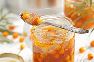 Jar of sea buckthorn jam. A spoonful of buckthorn jam close up. A pot, jam jar and sea buckthorn berries in the background