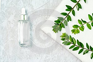 a jar of silver skin care cosmetics, a white towel and a sprig of luscious greenery