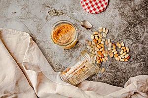 Jar and spoon of peanut butter and peanuts on dark wooden background from top view.Comfort food concept