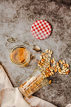 Jar and spoon of peanut butter and peanuts on dark wooden background from top view. Vegan and vegetarian food concept