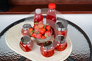 Jar with strawberry jam, raw strawberry in bowl, bottle with sirup on circle table
