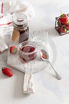 A jar of strawberry jam on a wooden board on white background. Close up, copy space for text or product. Tasty strawberry