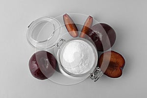 Jar with sweet fructose powder and ripe plums on white background, top view