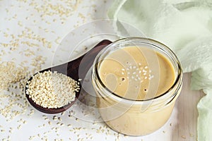 Jar of Tahini Sauce with Sesame Seeds in Wooden Spoon
