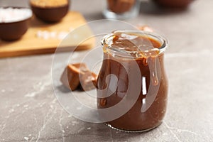 Jar with tasty caramel sauce on grey table