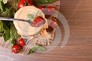 Jar of tasty tomato paste with spoon and ingredients on wooden table, flat lay. Space for text