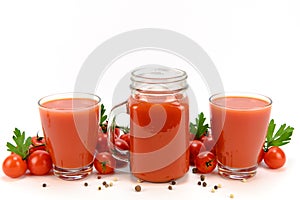 A jar and two glasses filled with tomato juice. Tomatoes, parsley and allspice peas lie around