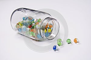 Jar of vintage glass marbles spilling onto a white background