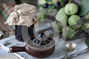Jar of walnut jam on a wooden table and a group of green walnuts