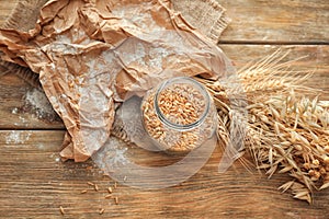 Jar with wheat grains and spikelets on wooden table
