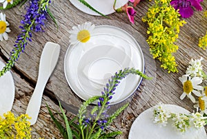 Jar with white face cream moisturizer, mask, ointment. Natural skin care concept. Old wooden background with field flowers.