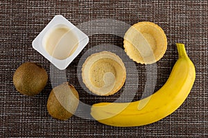 Jar with yogurt, kiwi and banana, tartlets on mat. Top view