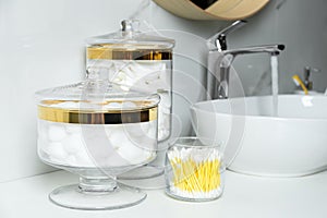 Jars with cotton balls, swabs and pads on countertop in bathroom