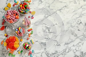 Jars with different delicious candies on white marble table, flat lay. Space for text