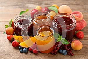 Jars with different jams and fresh fruits on wooden table