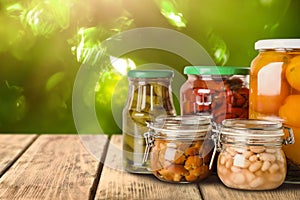 Jars of different pickled foods on wooden table against blurred background, space for text