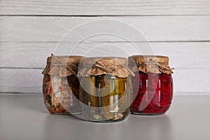 Jars with different preserved vegetables on light grey table