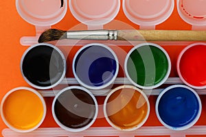 Jars of gouache on an orange background. Set for the development of creativity