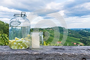 Jars with grapes and candle on wooden bench near vineyard along