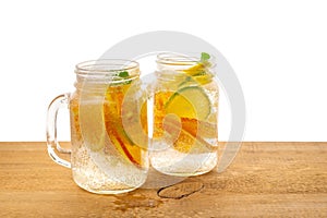Jars of homemade lemonade with sliced fresh lemon, orange, lime, twig mint and bubbles on wooden background isolated, detox fruit