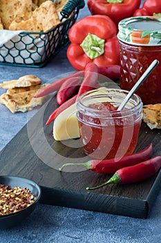 Jars of hot pepper jelly surrounded by peppers, cracker bread and cheese.