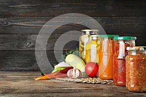 Jars with pickled products and fresh vegetables on wooden table against black background