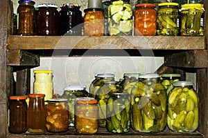 Jars pickled vegetables, fruity compotes and jams in cellar. Preserved food photo