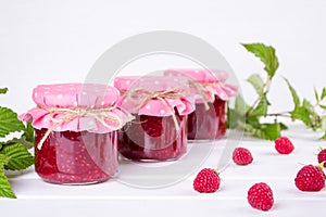 Jars with raspberry jam placed in rows and fresh raspberry