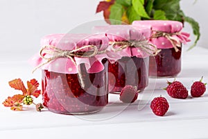 Jars with raspberry jam placed in rows and fresh raspberry