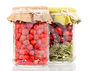Jars with rowan berries and rose hips on white.