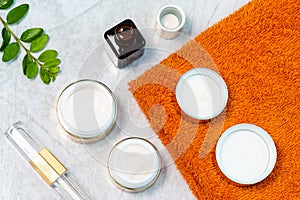 jars of skin care cosmetics in gold colour, an orange towel and a sprig of luscious greenery