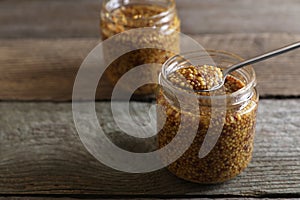 Jars and spoon of whole grain mustard on wooden table, closeup. Space for text