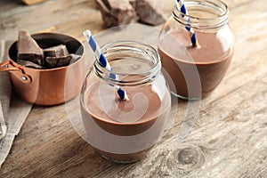 Jars with tasty chocolate milk on wooden table.