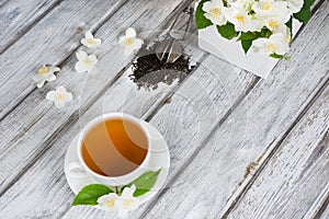 Jasmine dry green tea leaves with fresh jasmine flowers and white cup of green tea on wooden background. Top view.