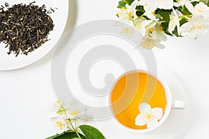 Jasmine dry green tea leaves with jasmine flowers and cup of tea on white background. Copy space and top view. Teatime.