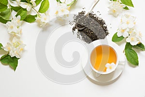 Jasmine dry green tea leaves with jasmine flowers and cup of tea on white background. Copy space and top view. Teatime.