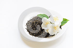 Jasmine dry green tea on white plate with decor from jasmin flowers on white background. Side view.