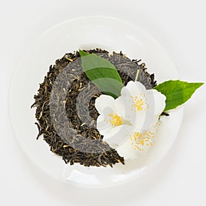 Jasmine dry green tea on white plate with decor from jasmin flowers on white background. Top view.